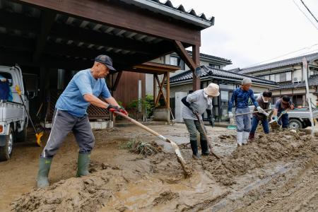 石川県羽咋市で住宅に流れ込んだ泥を道路に出す人たち=28日午前