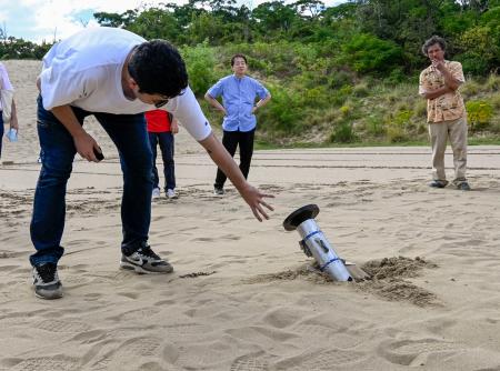 　鳥取砂丘の地中に打ち込まれたロケット型の機器を確認する研究チームの学生＝２日午後、鳥取市