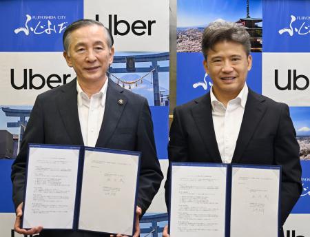 包括連携の協定書を手にする山梨県富士吉田市の堀内茂市長（左）とウーバージャパンの山中志郎代表＝４日午前、富士吉田市役所