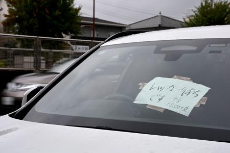 　フロントガラスに紙が張られた、大雨で被災し路上に残された車両＝９日午前９時２０分、名古屋市千種区
