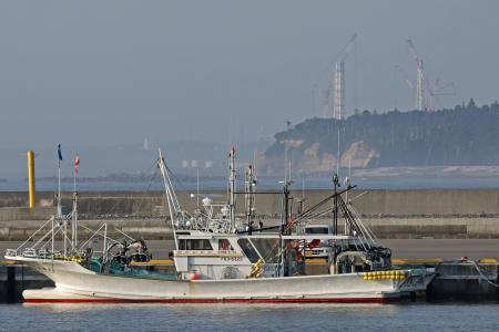 　福島県浪江町の請戸漁港に停泊する漁船。奥は東京電力福島第１原発の排気筒＝２０２４年８月